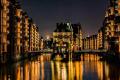 Mond fotografieren mit Vordergrund – Hamburger Speicherstadt bei Nacht Mondsichel über der Hamburger Speicherstadt mit beleuchtetem Wasserschloss und goldenen Lichtreflexionen im Wasser.